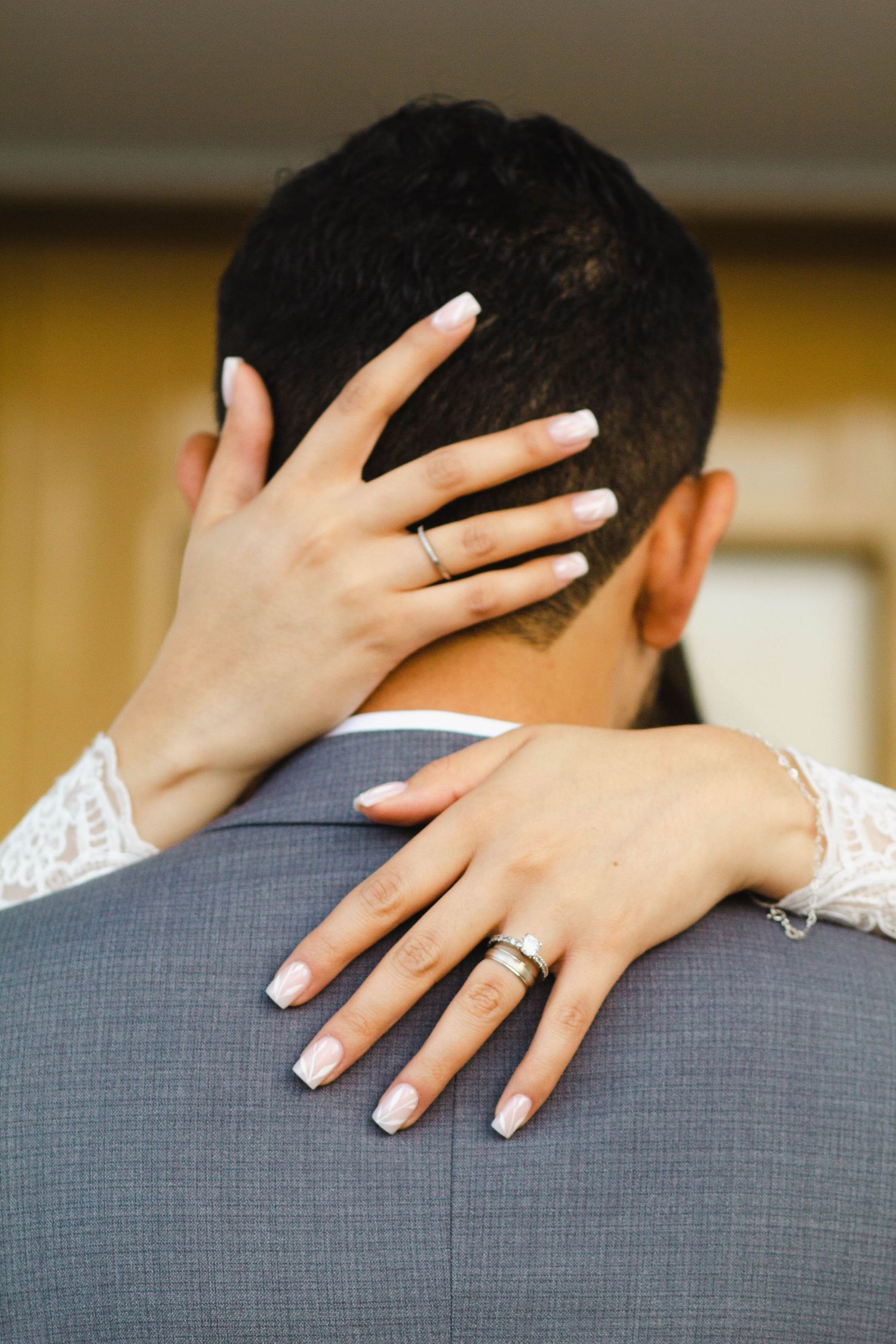 Close-up of hands with wedding rings embracing from behind.