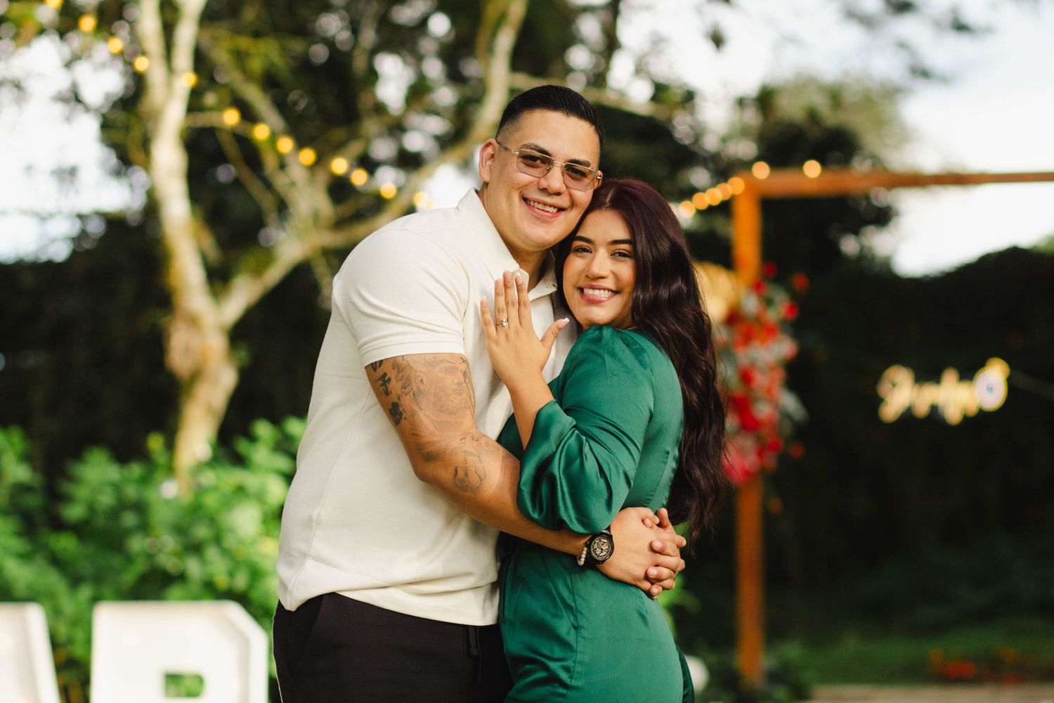 An engaged couple embraces joyfully outdoors in coordinating white and green outfits.