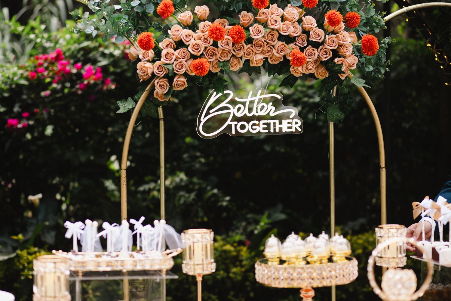 Elegant outdoor wedding reception setup with peach roses, crystal chandeliers and white decor elements under natural greenery.