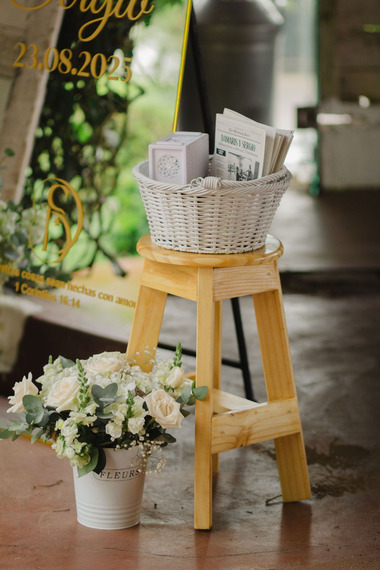A wooden stool displays a white wicker basket and floral arrangement in white and green tones for event decor.