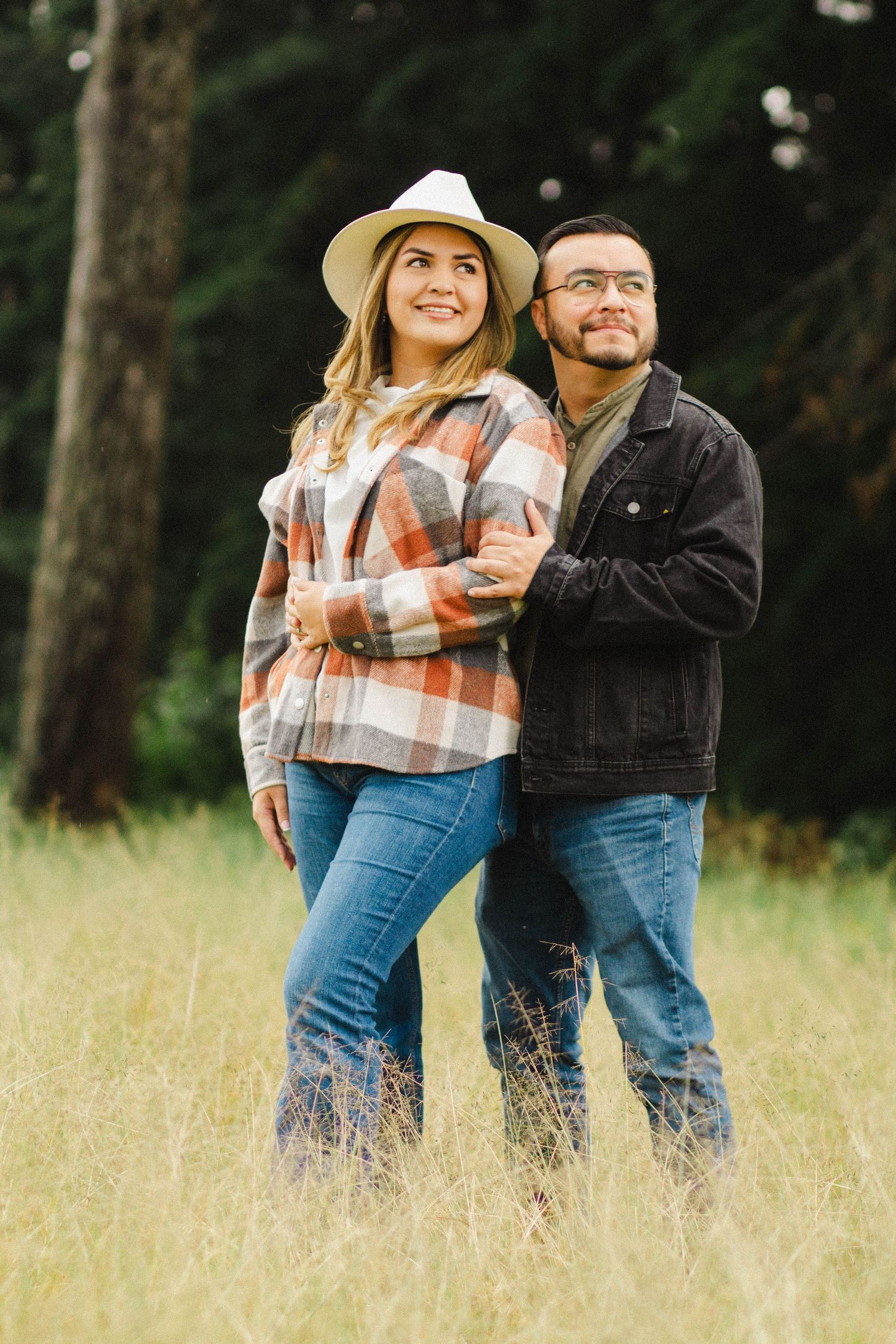Couple in matching plaid and denim posing in tall grass field.