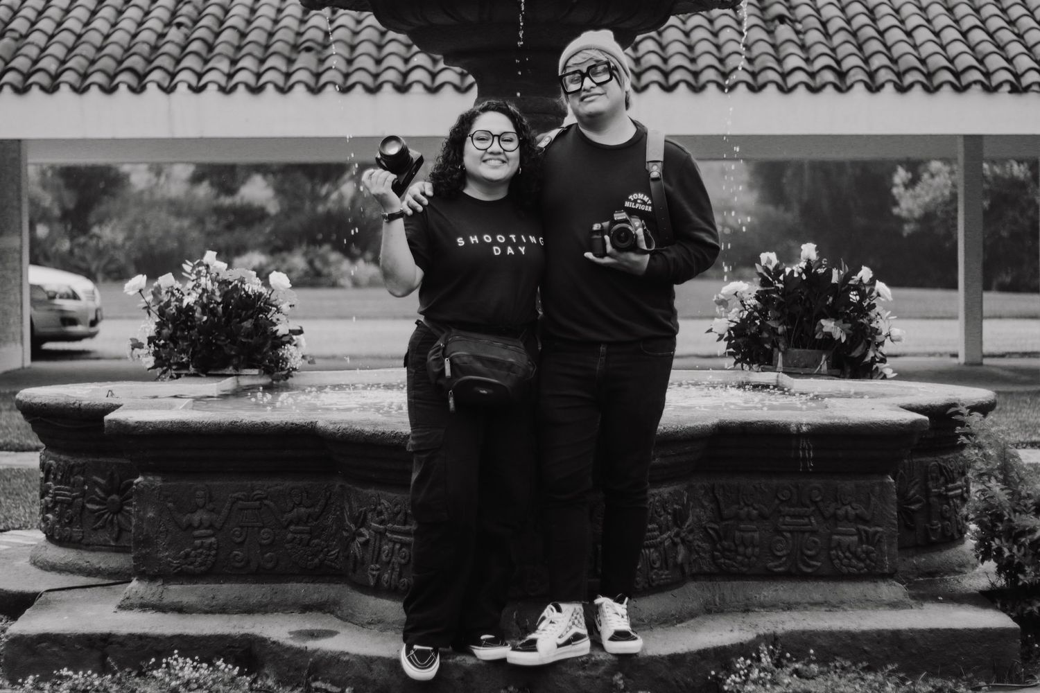 A couple poses together in front of a brick wall and landscaping in a series of black and white engagement photos.