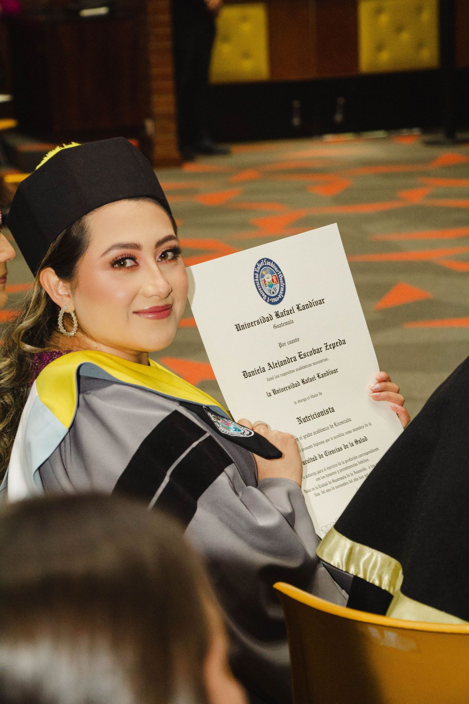 Graduate in academic regalia proudly displays diploma certificate during graduation ceremony.