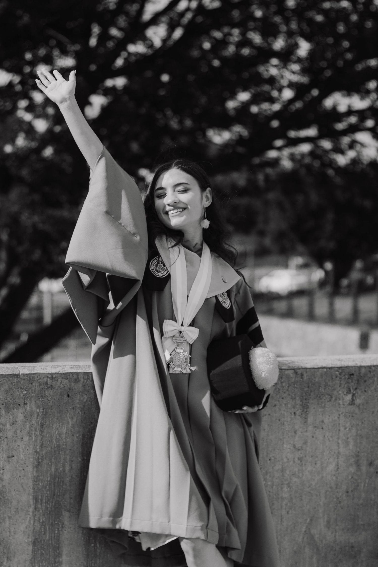 Graduate celebrating with raised arm while wearing academic regalia in black and white photo.