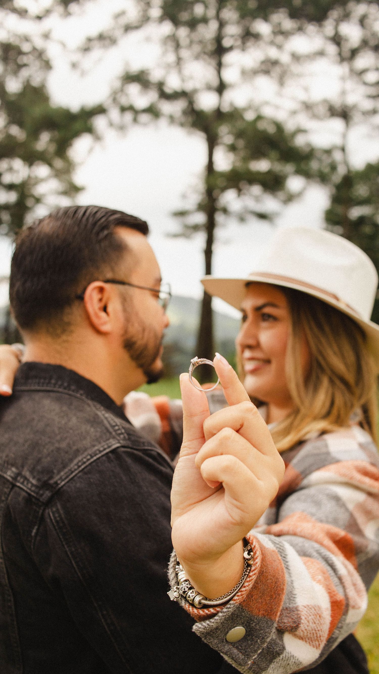 Couple in casual wear showing off engagement ring in outdoor setting.