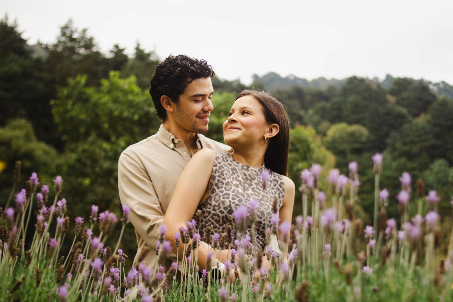 A couple shares a romantic moment while standing in a lavender field with lush greenery in the background.
