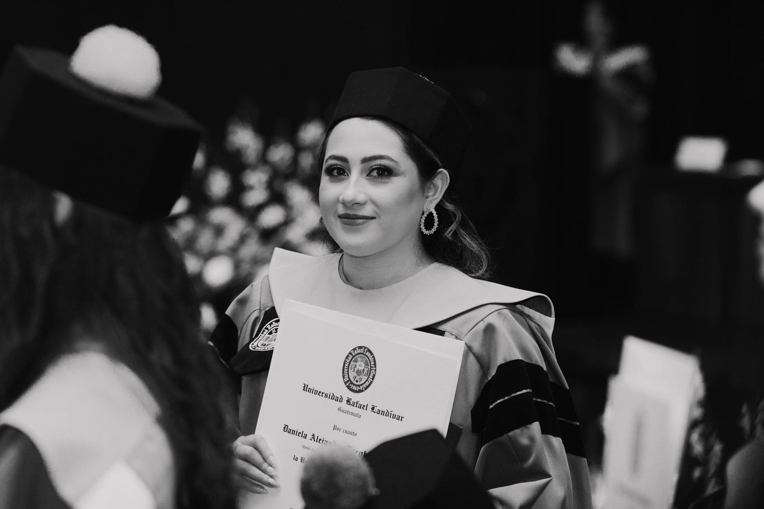 A graduate holds their diploma during a graduation ceremony in black and white photography.