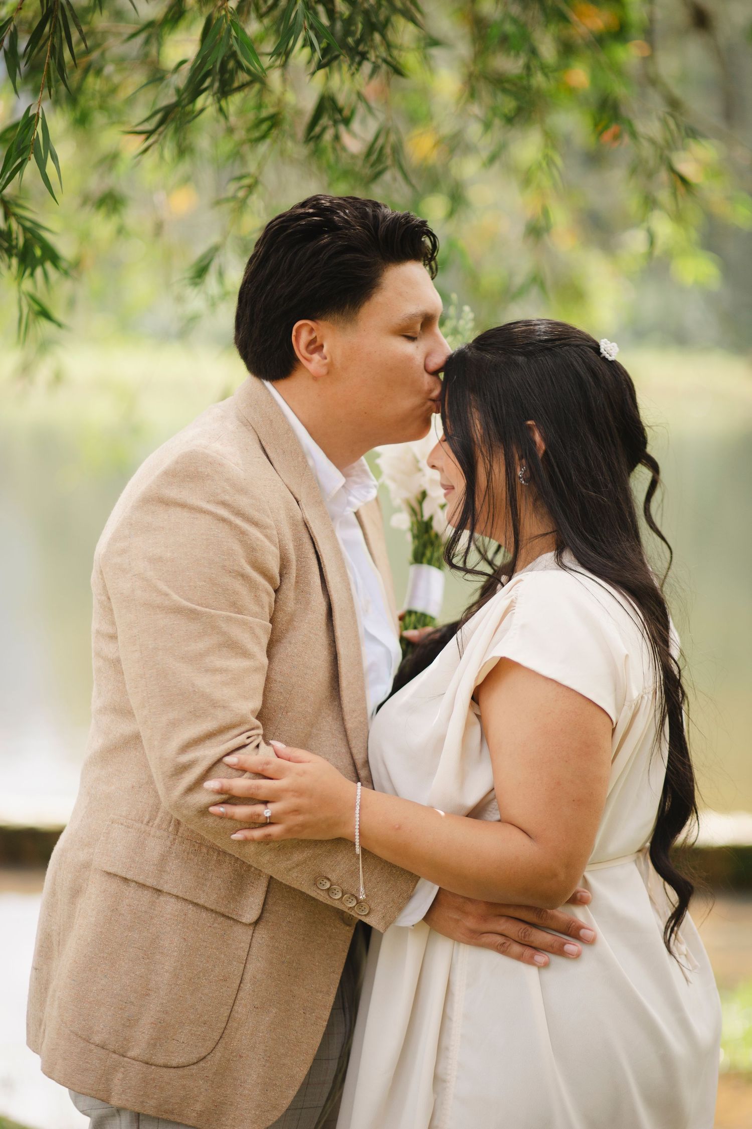 A romantic couple shares tender kisses in a garden setting while wearing beige and white outfits.