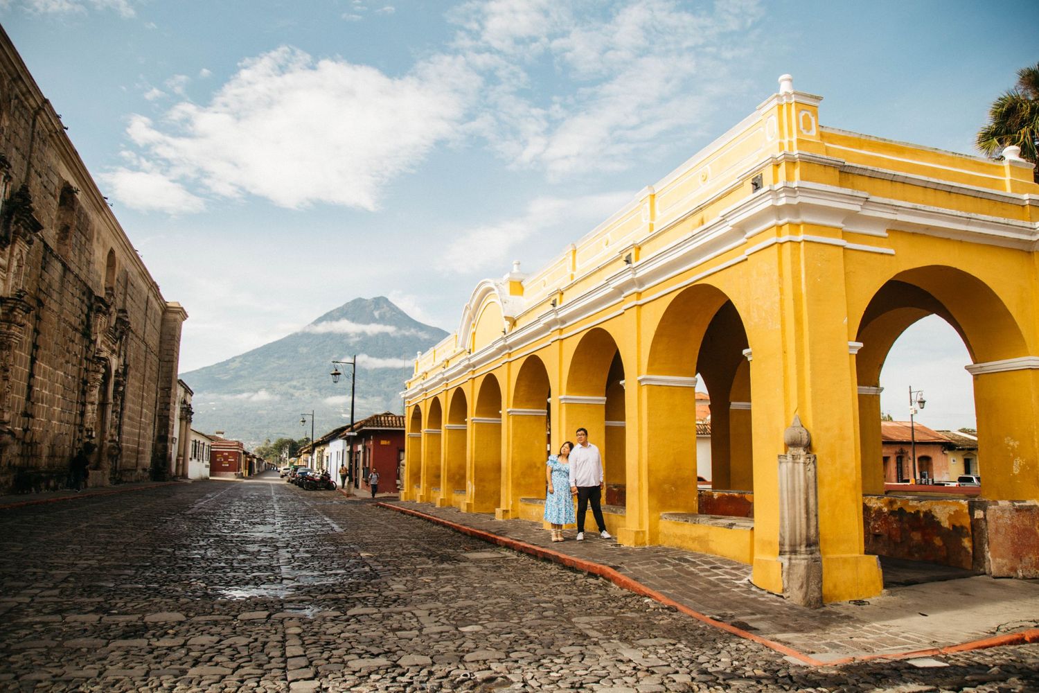 Yellow colonial arches and cobblestone street with volcano vista in Antigua Guatemala.