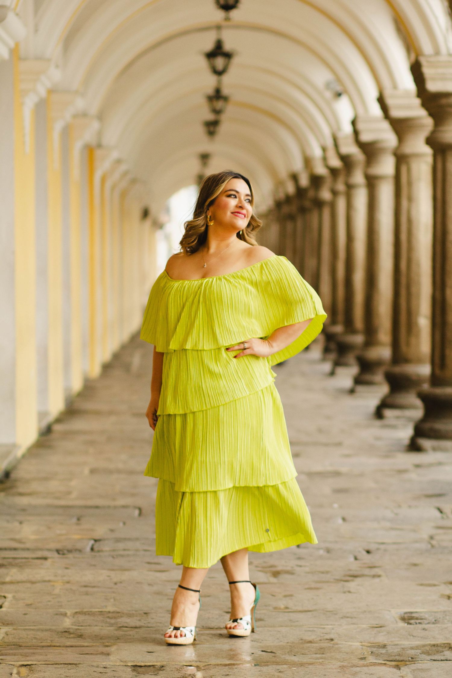 Woman in a bright yellow tiered dress posing in an elegant archway corridor.