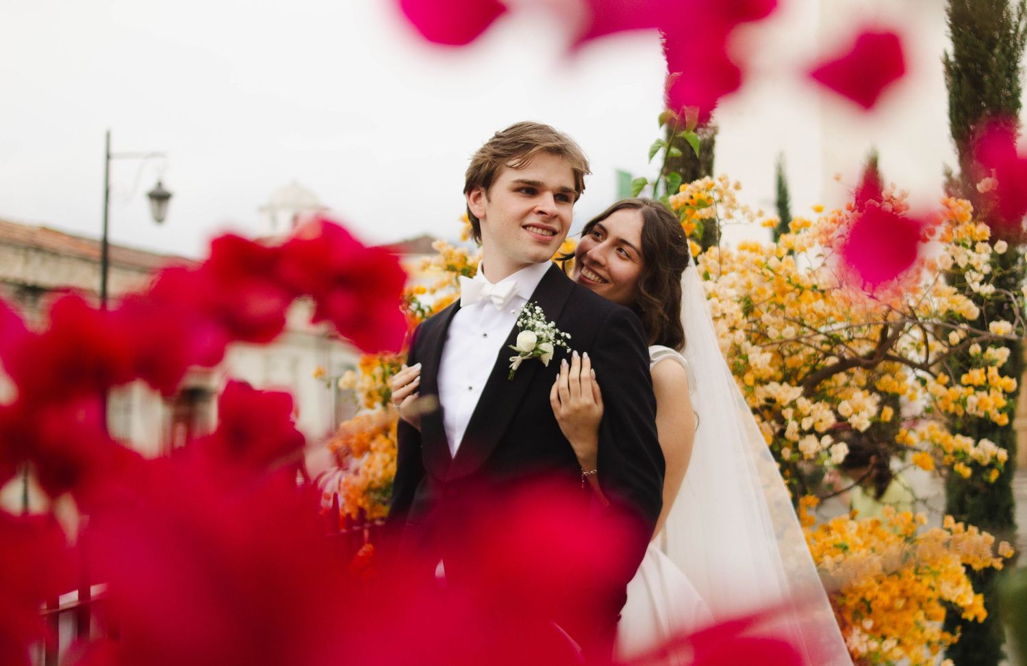 Wedding couple celebrates through frame of red flowers in romantic outdoor setting..
