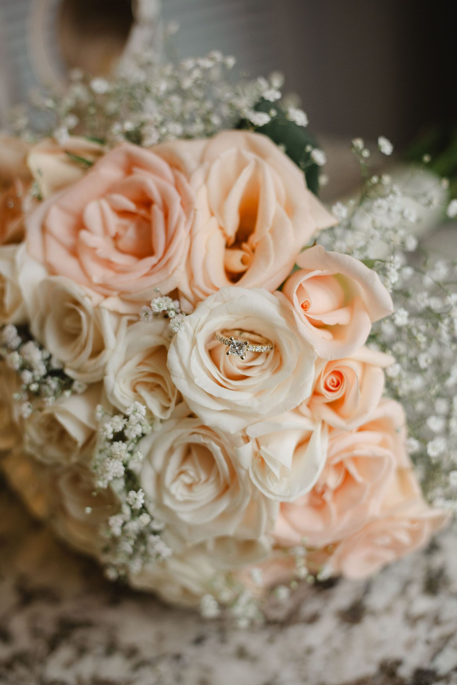 A close-up series of peach and cream colored roses with baby's breath flowers and wedding rings nestled among the petals.