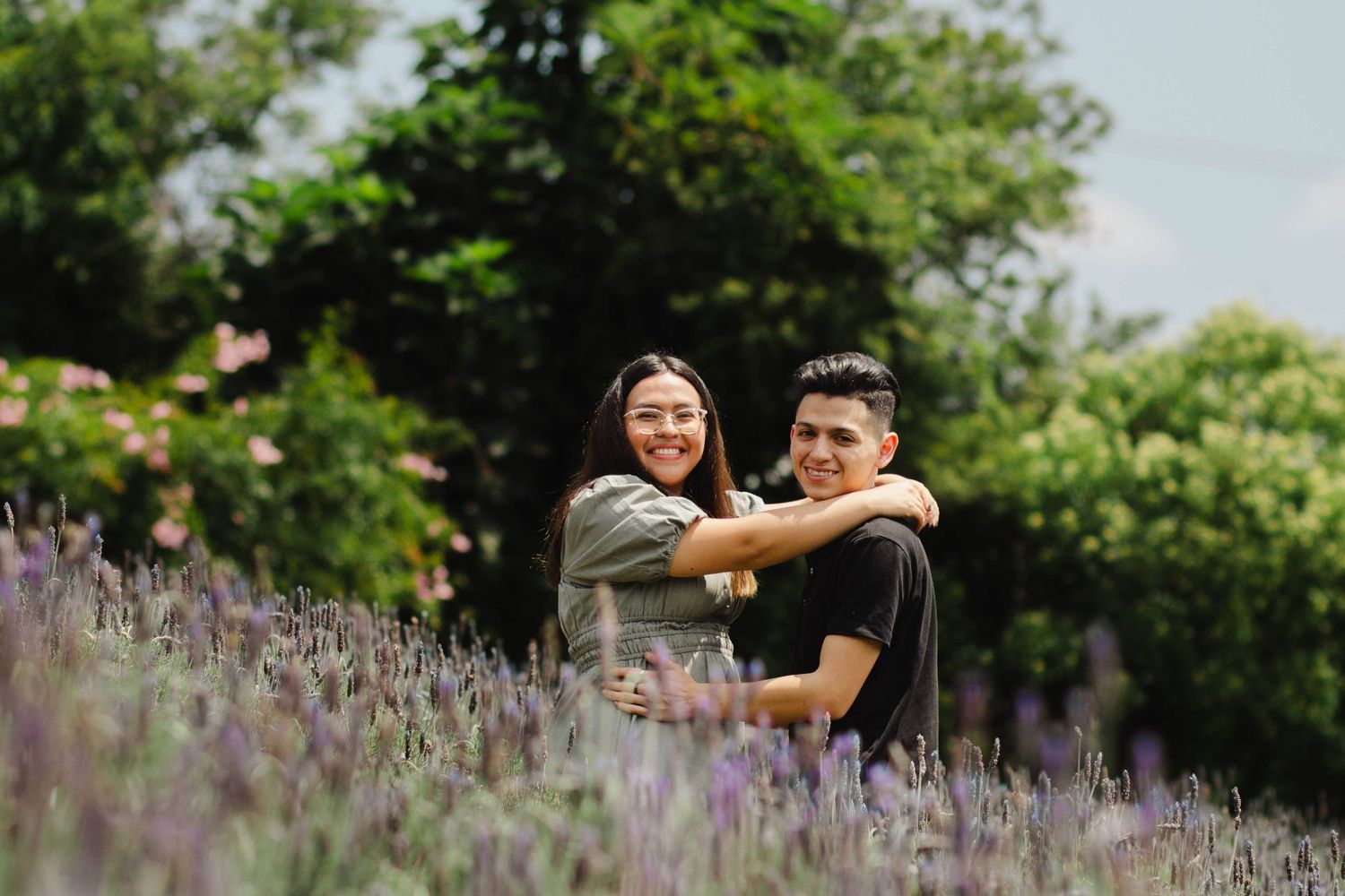 Couple embracing in field of purple lavender flowers with green foliage background.