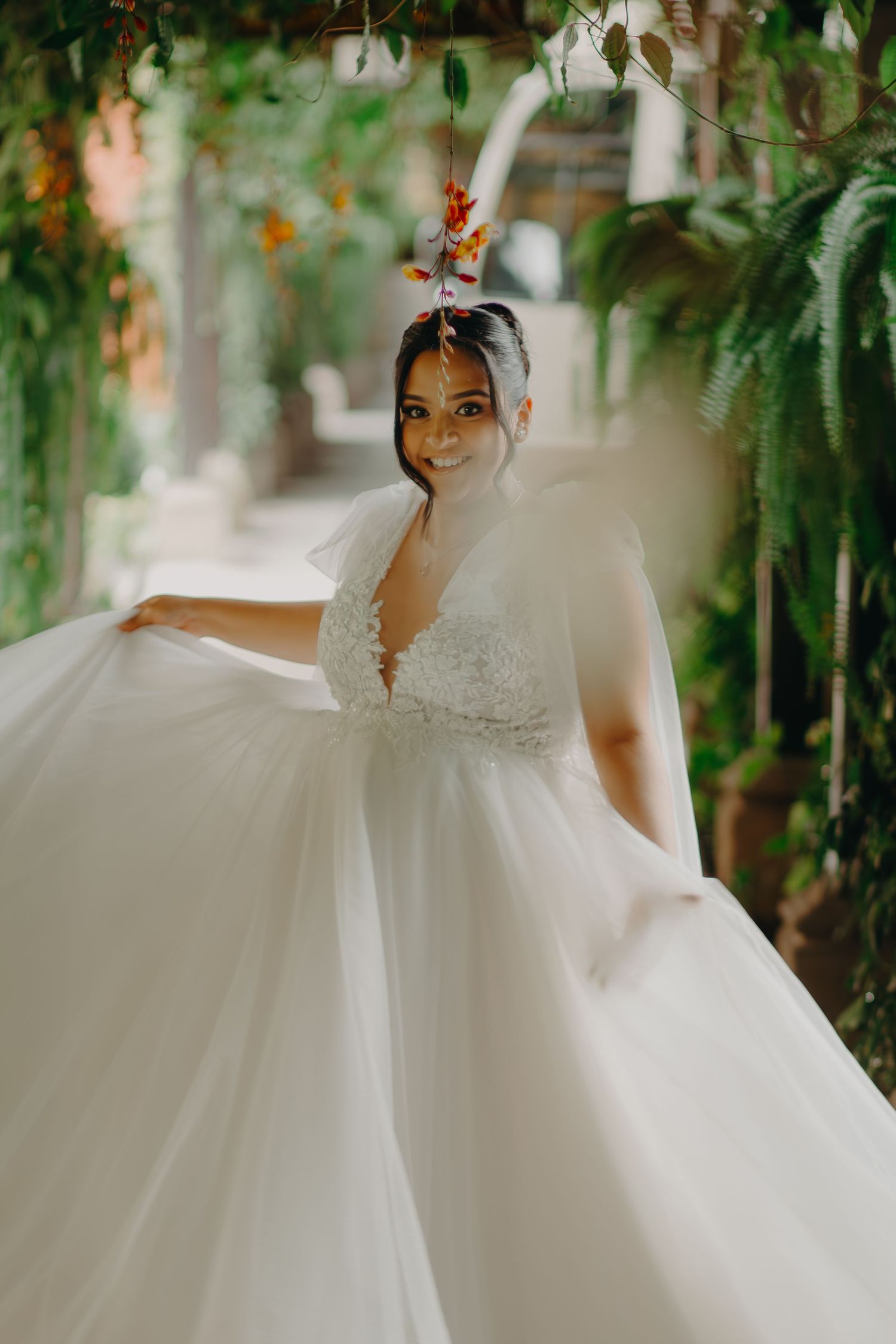 A bride in a luxurious white ball gown stands among lush greenery in an elegant garden setting.