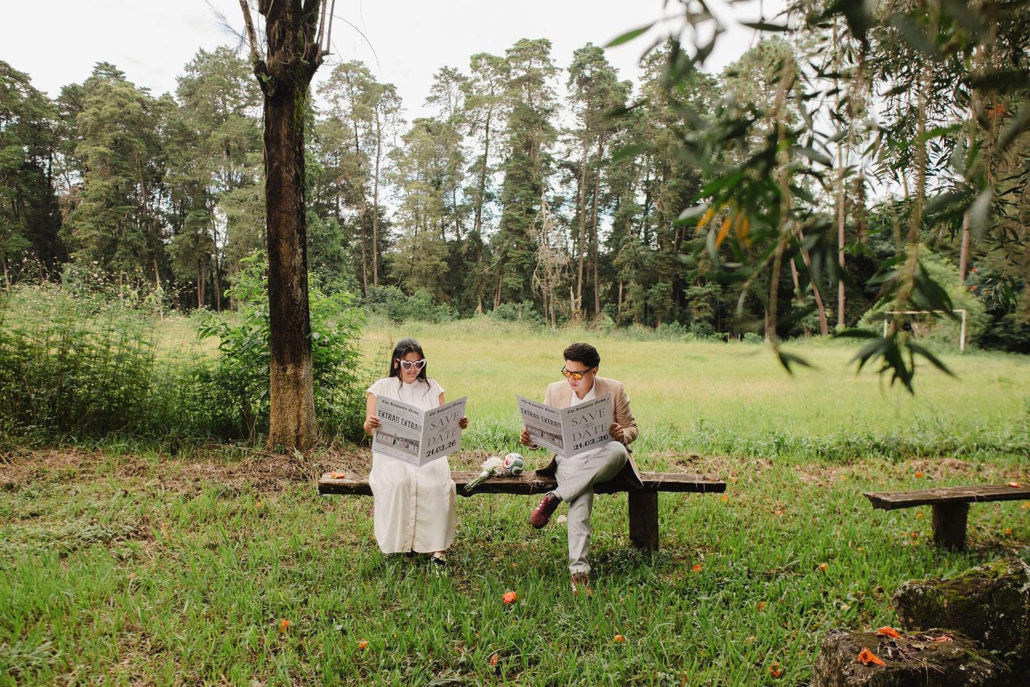 A couple sits together on a wooden bench in a lush green park setting reading newspapers on a peaceful afternoon.