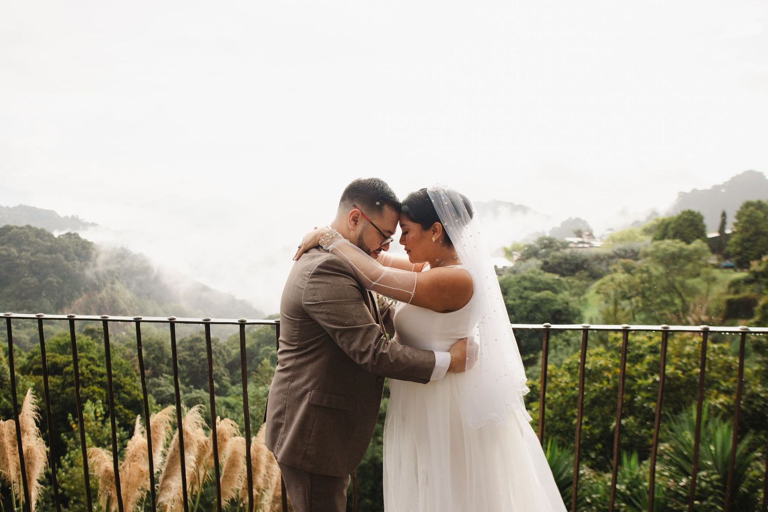 A couple embraces during their wedding ceremony overlooking a scenic mountain landscape on a misty day.