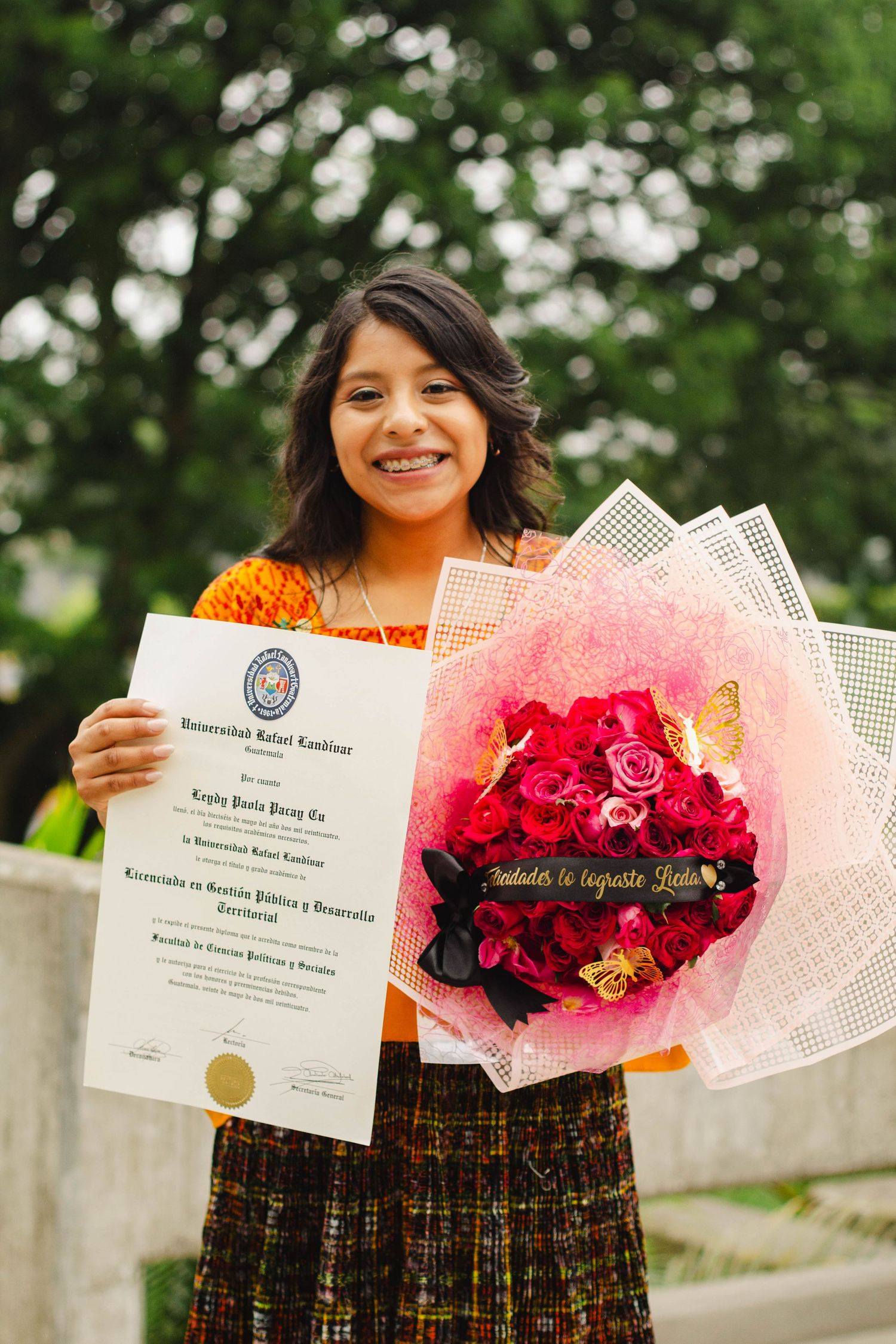 Graduate holds diploma and beautiful red rose bouquet while celebrating outdoors.