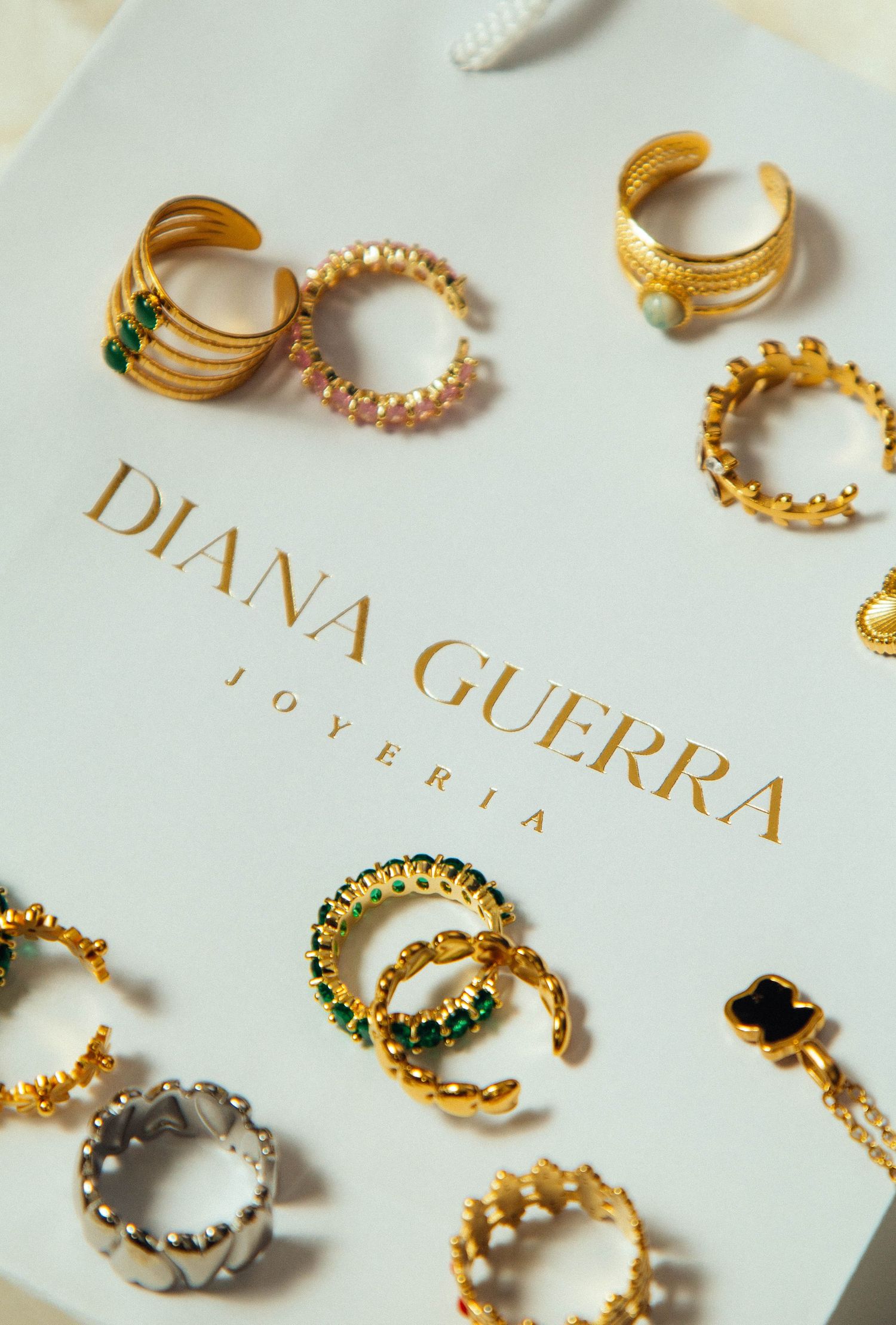 Collection of delicate gold and crystal rings displayed on a Diana Guerra jewelry branding card.