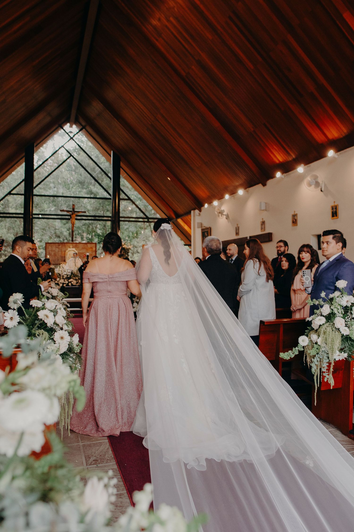 Wedding ceremony in a rustic chapel with vaulted wooden ceiling and elegant white floral decorations.