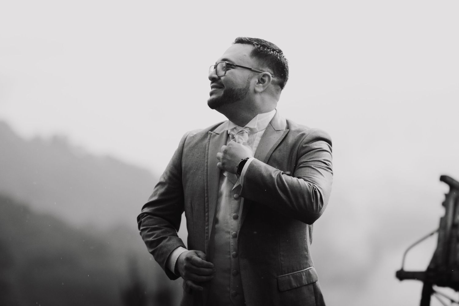 Black and white photo of person in suit jacket looking off into misty mountains with contemplative expression.