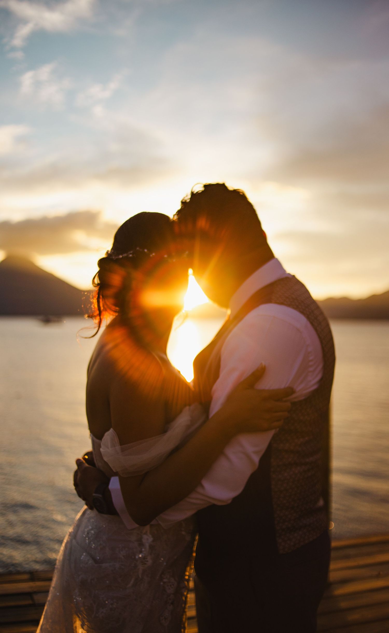 Silhouetted couple embracing at sunset by a waterfront.