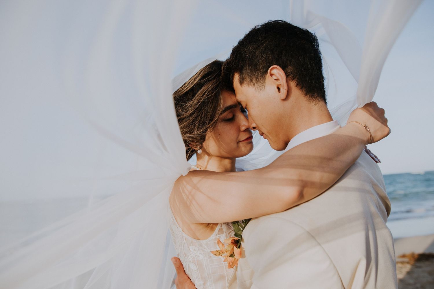 Romantic couple in white embracing on a beach at sunset with ocean waves in background.