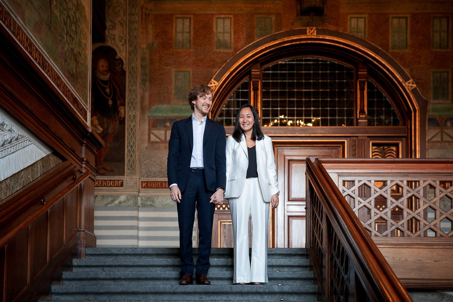 A couple poses elegantly on ornate vintage stairs in formal attire.