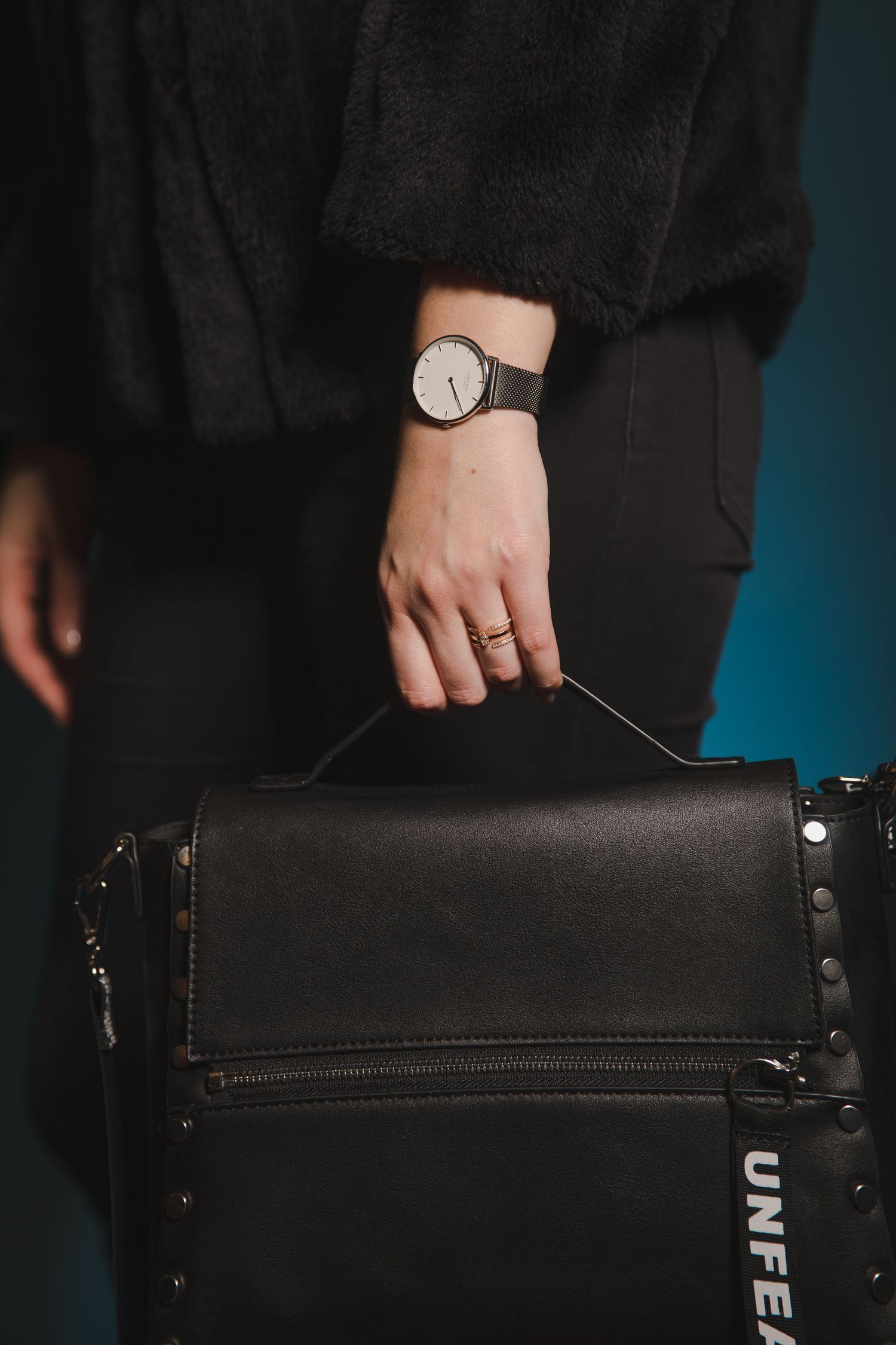 Close-up of a hand wearing a watch and ring while holding a black leather bag.