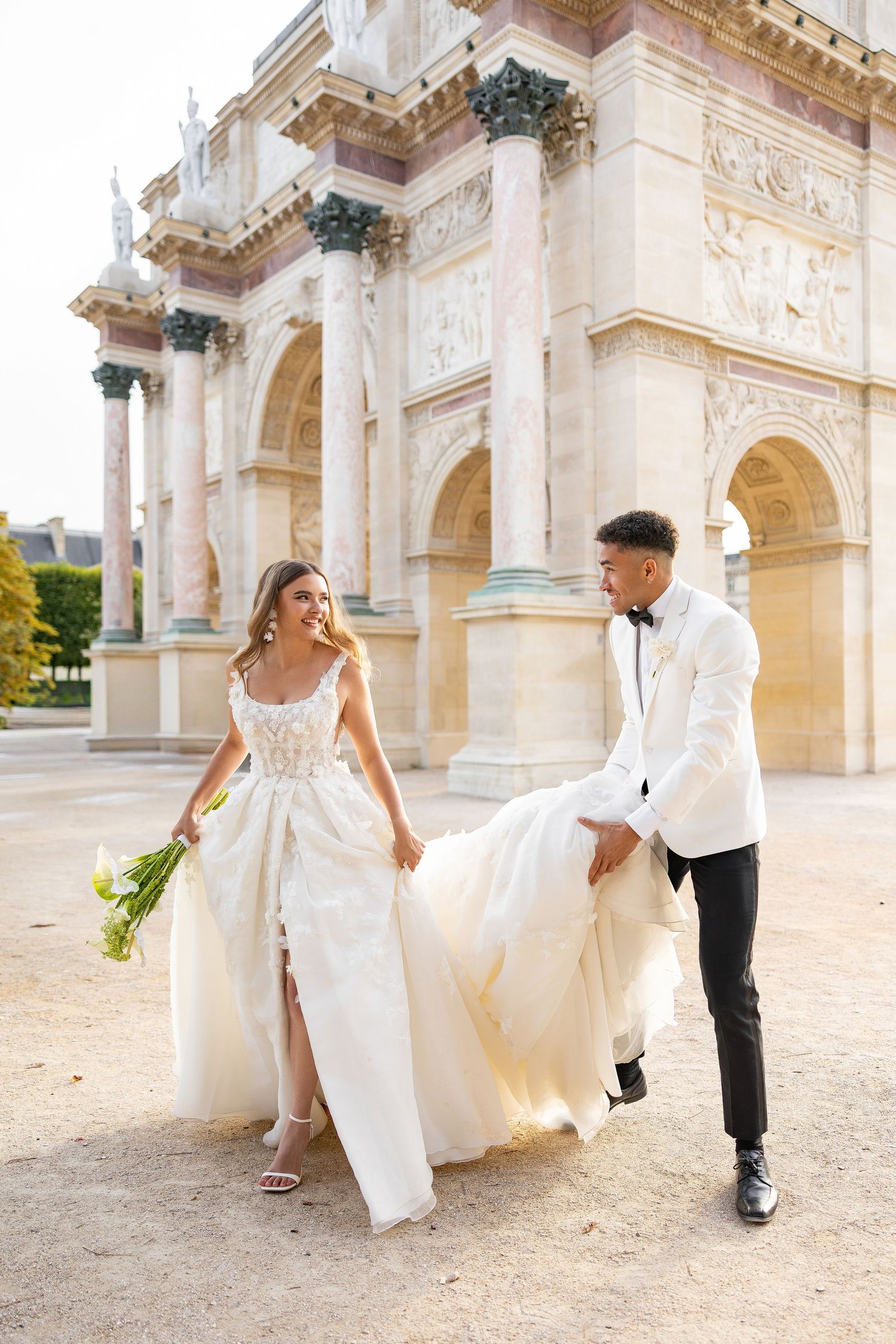 Newlyweds share joyful moment in front of grand architectural backdrop.