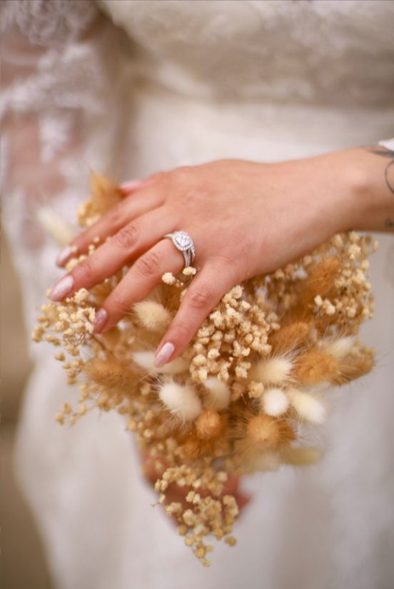 Hand gently holding dried baby's breath flowers against a soft white background.