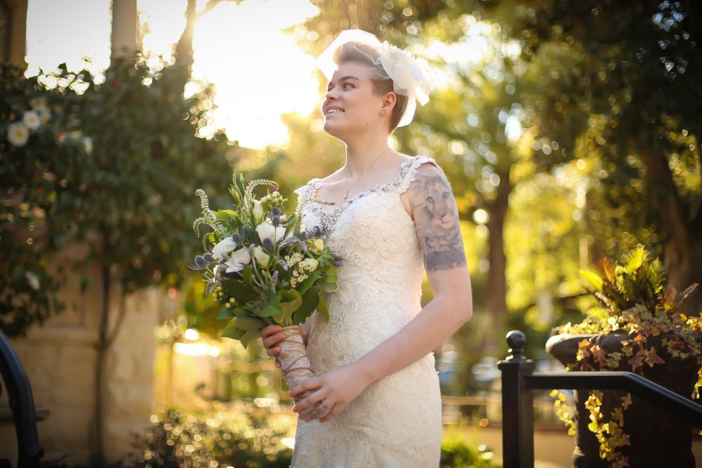 A person in a white wedding dress poses in golden sunlight among trees.
