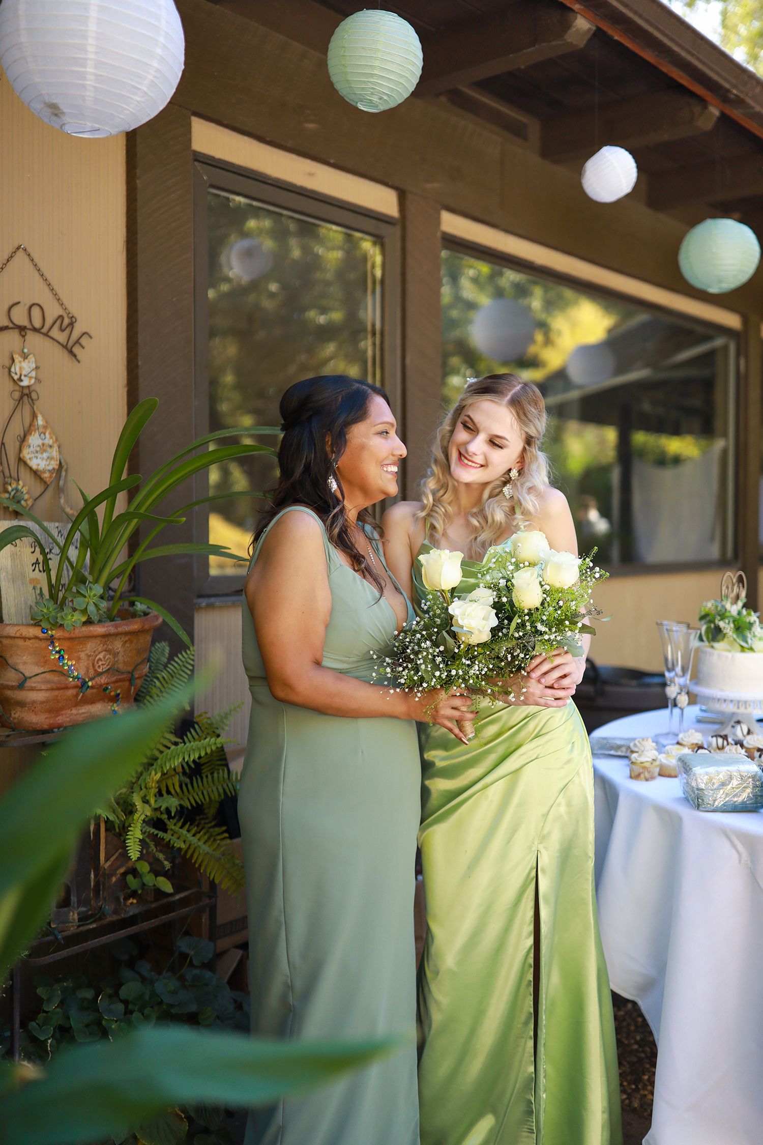 Two people in mint green dresses share a joyful moment at a reception with paper lanterns.