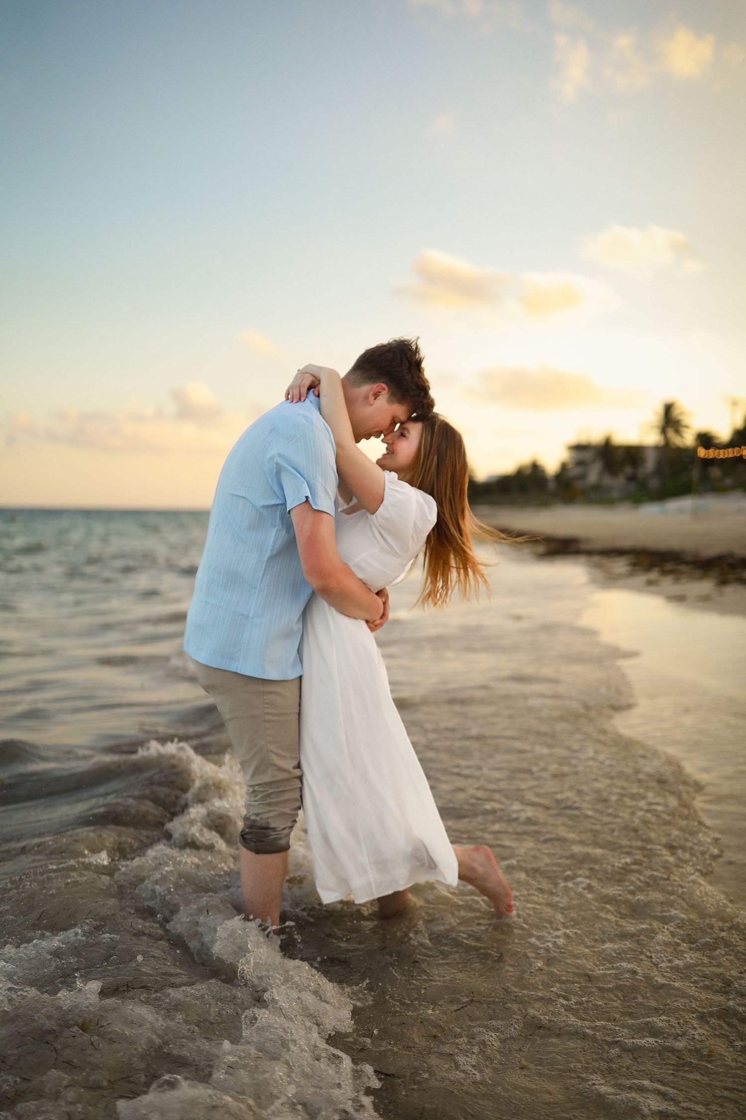 Romantic couple embracing in shallow ocean water during sunset photoshoot.