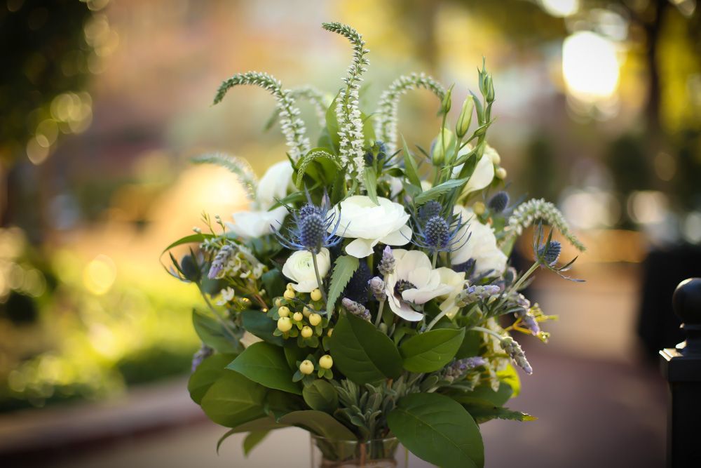 Wedding floral centerpiece with white roses and greenery glows in soft evening light at an outdoor reception table.