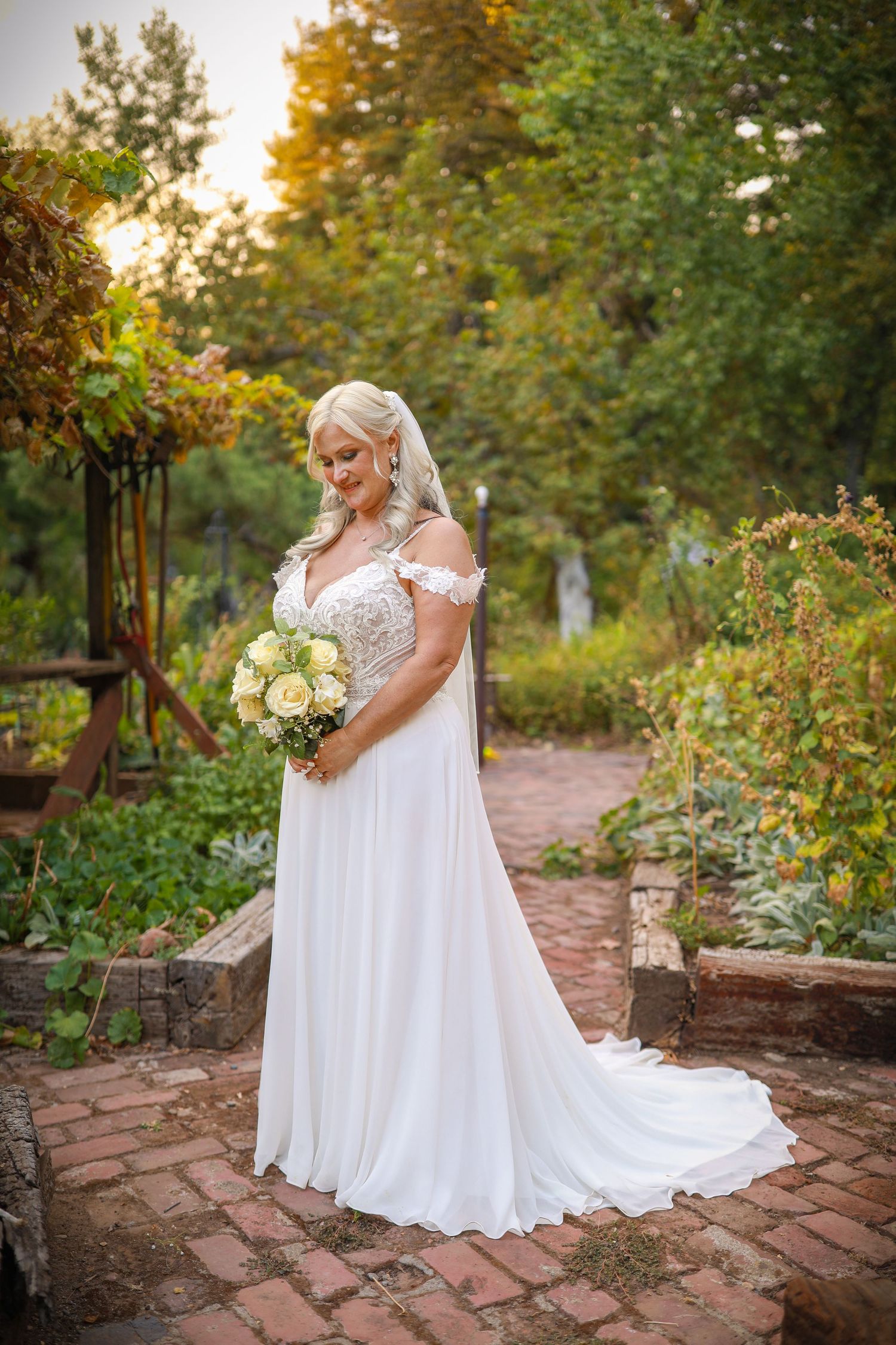Bride in a flowing white wedding gown poses in a garden setting at sunset.