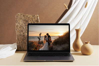 Laptop displaying beach family photo on wooden desk with decorative items and neutral background.