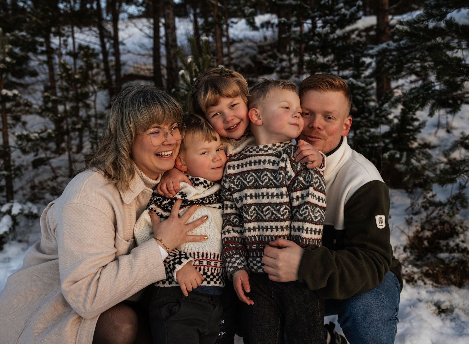 Happy family of five posing outdoors in snowy winter forest, parents and three children wearing cozy sweaters.