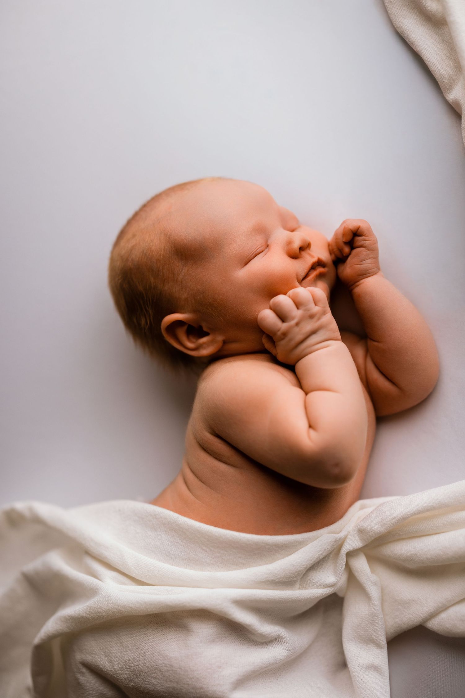Peaceful newborn baby sleeping on white blanket with tiny hands near face in serene portrait.