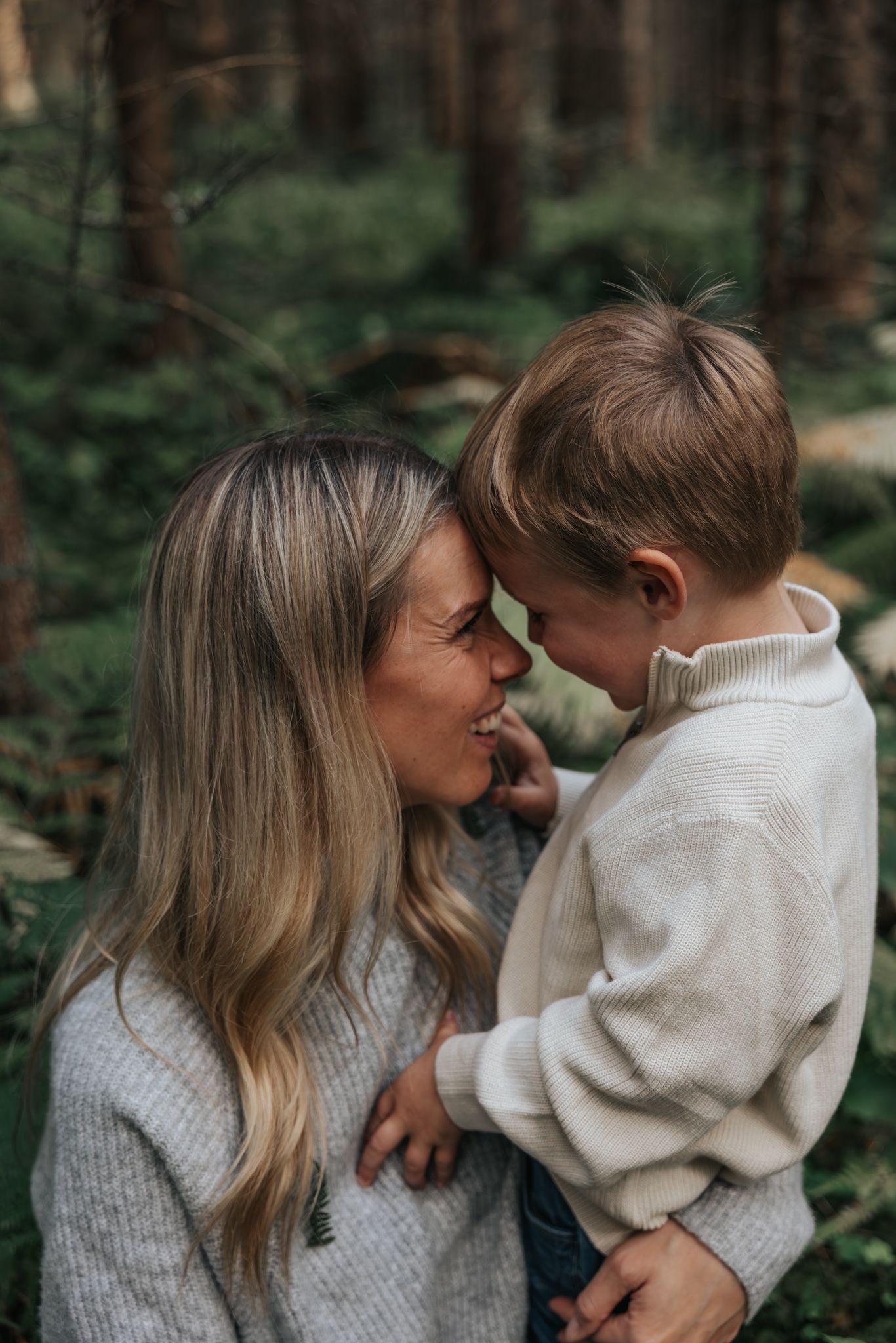 Mother and young son sharing a tender forehead-to-forehead moment in the woods.