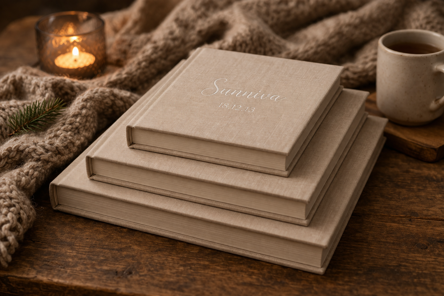 Three stacked linen-covered photo albums of different sizes on a wooden table with warm candlelight ambiance.