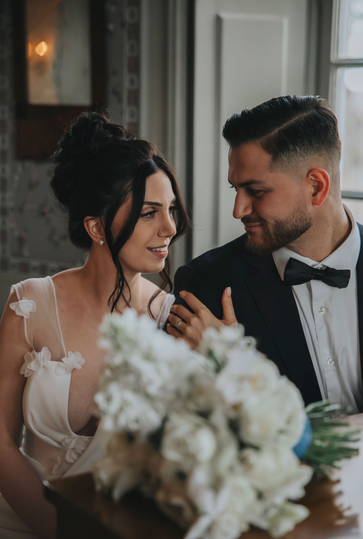 A bride and groom share an intimate moment at their wedding reception, with white floral arrangements in the foreground.