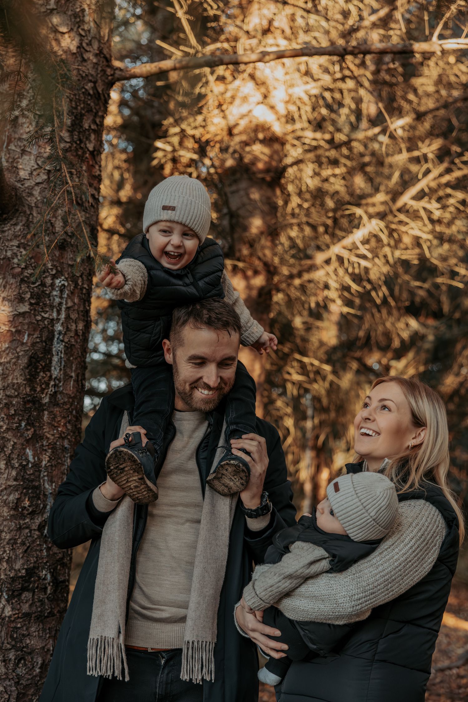 A smiling family in autumn forest with toddler on fathers shoulders and baby in mothers arms.
