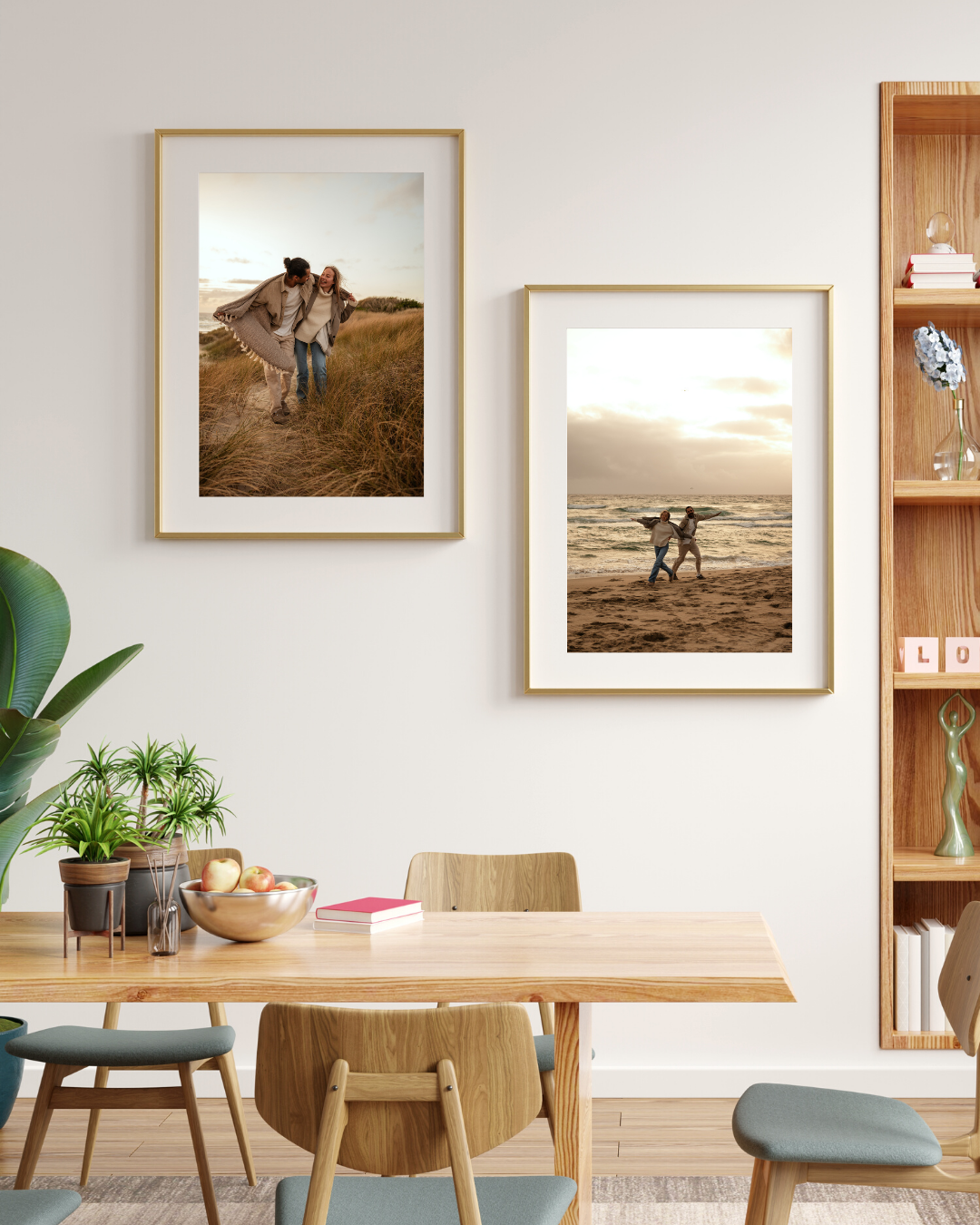 Two framed family beach photos displayed on a white dining room wall with wooden furniture and green plants.