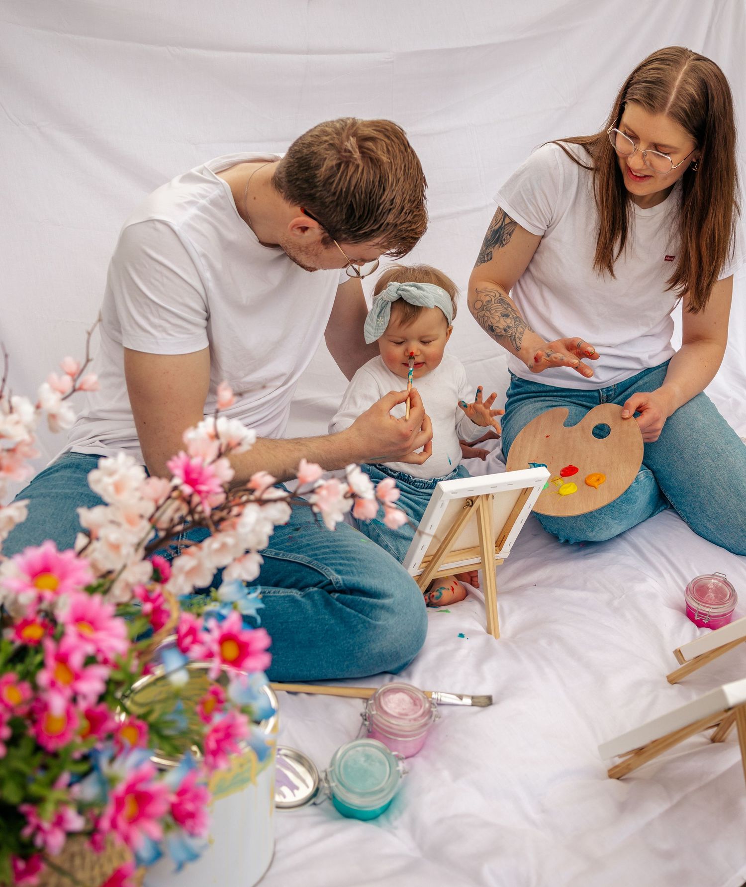 A young family sitting together painting with a baby surrounded by pink flowers.