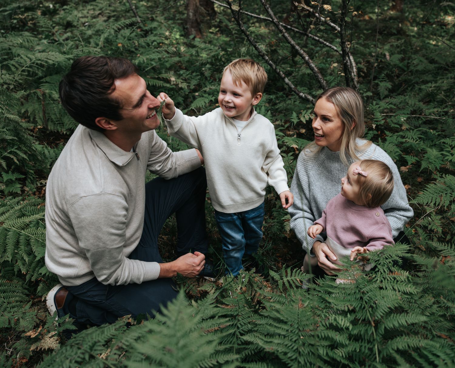 Happy family with two young children playing among ferns in a lush green forest.