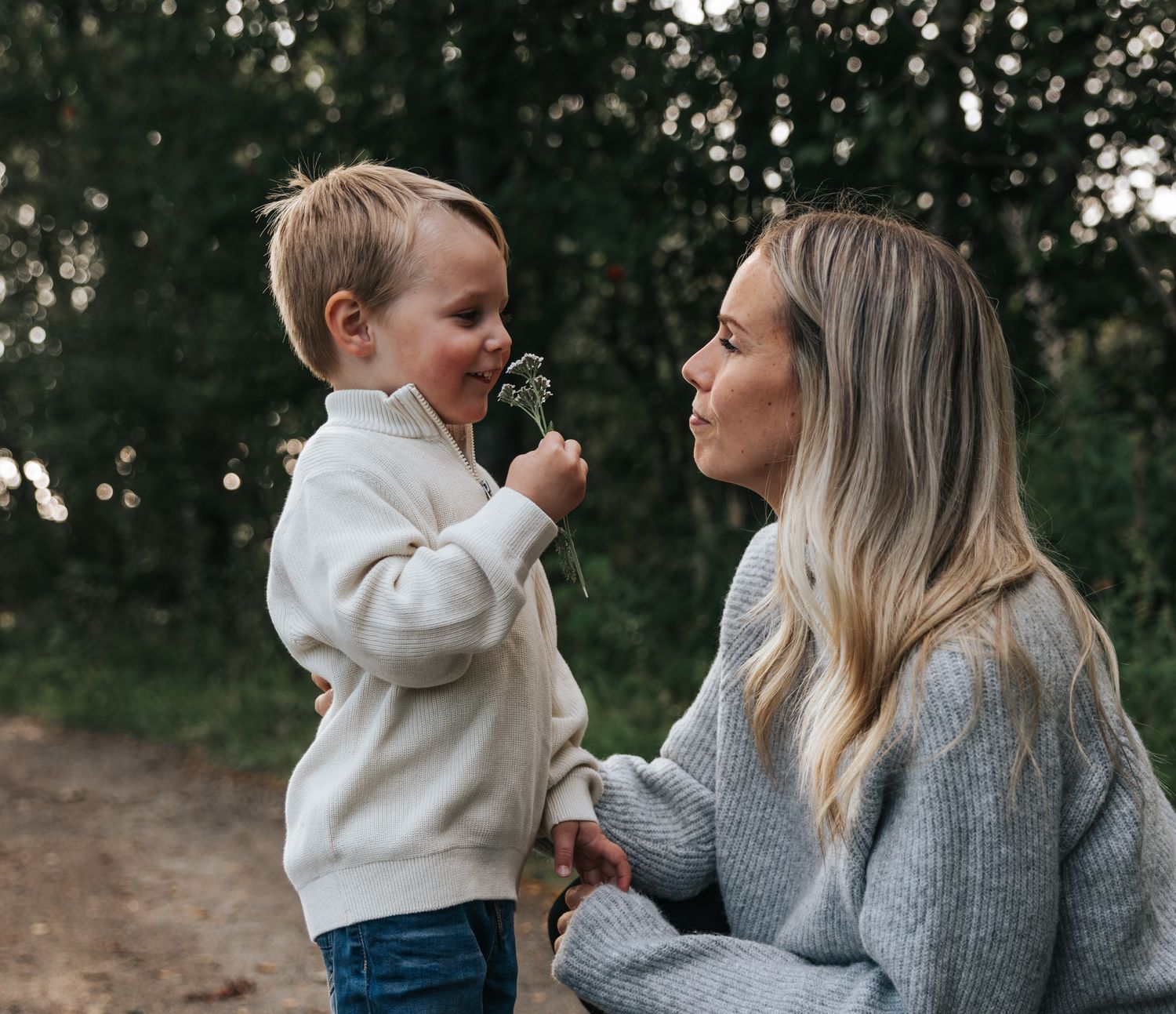 Young boy offering a flower to his smiling blonde mother outdoors in nature.