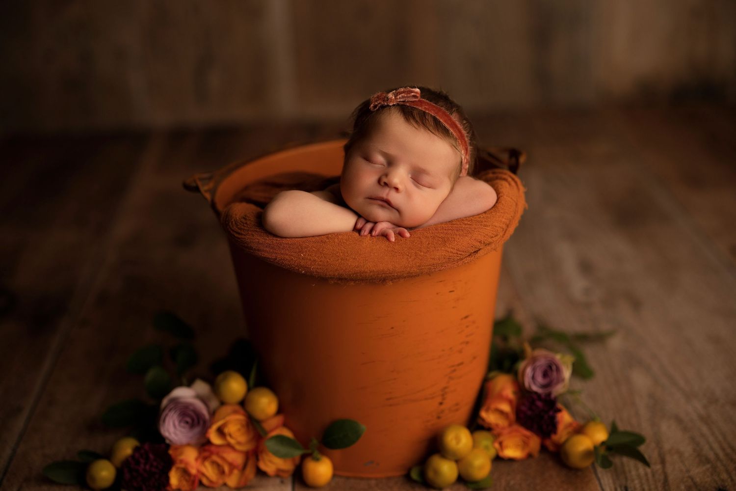 Newborn baby girl sleeping in a terracotta pot surrounded by colorful flowers.