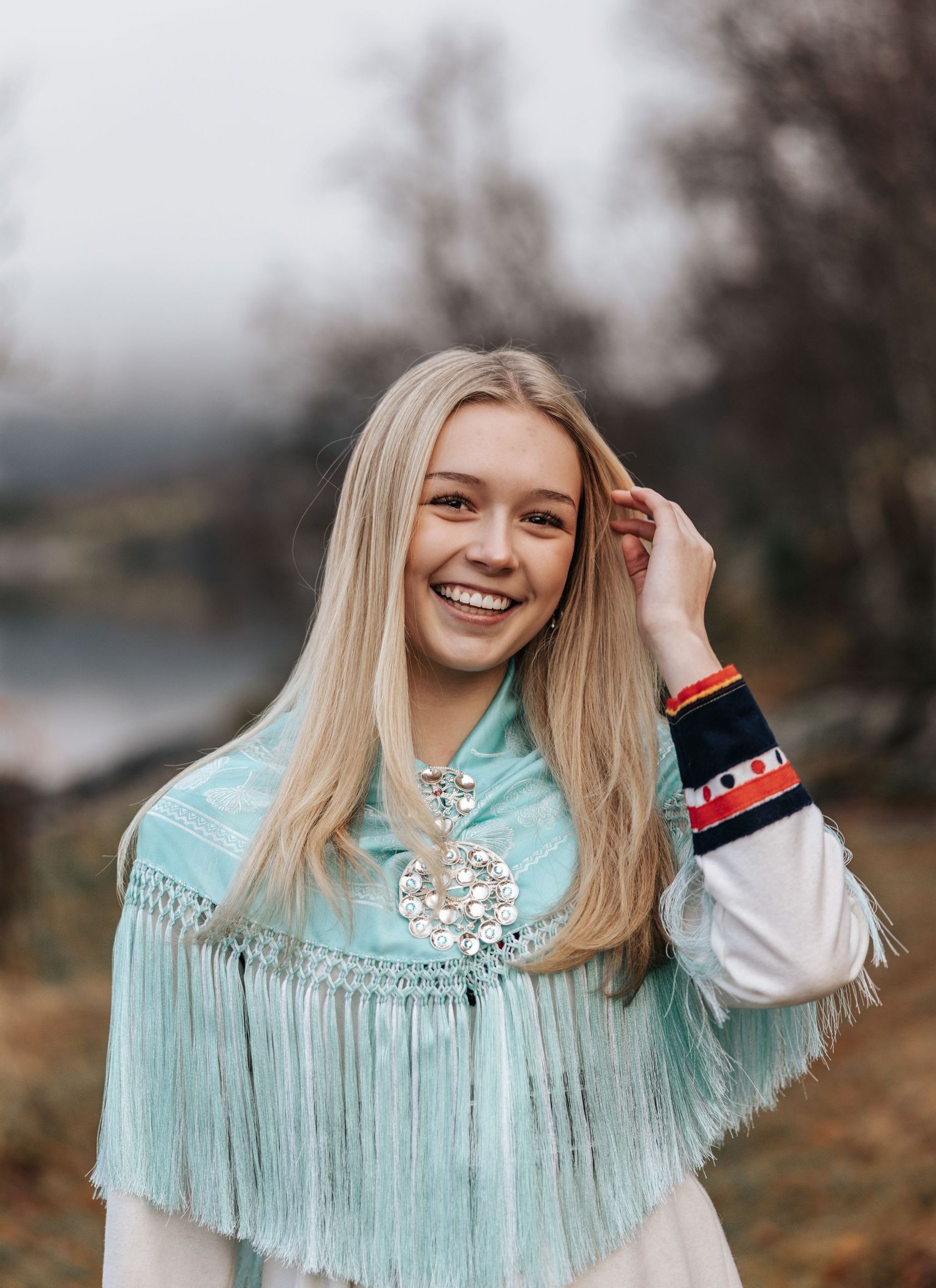 Smiling blonde teenage girl wearing a traditional Norwegian bunad with a turquoise shawl and silver brooch.