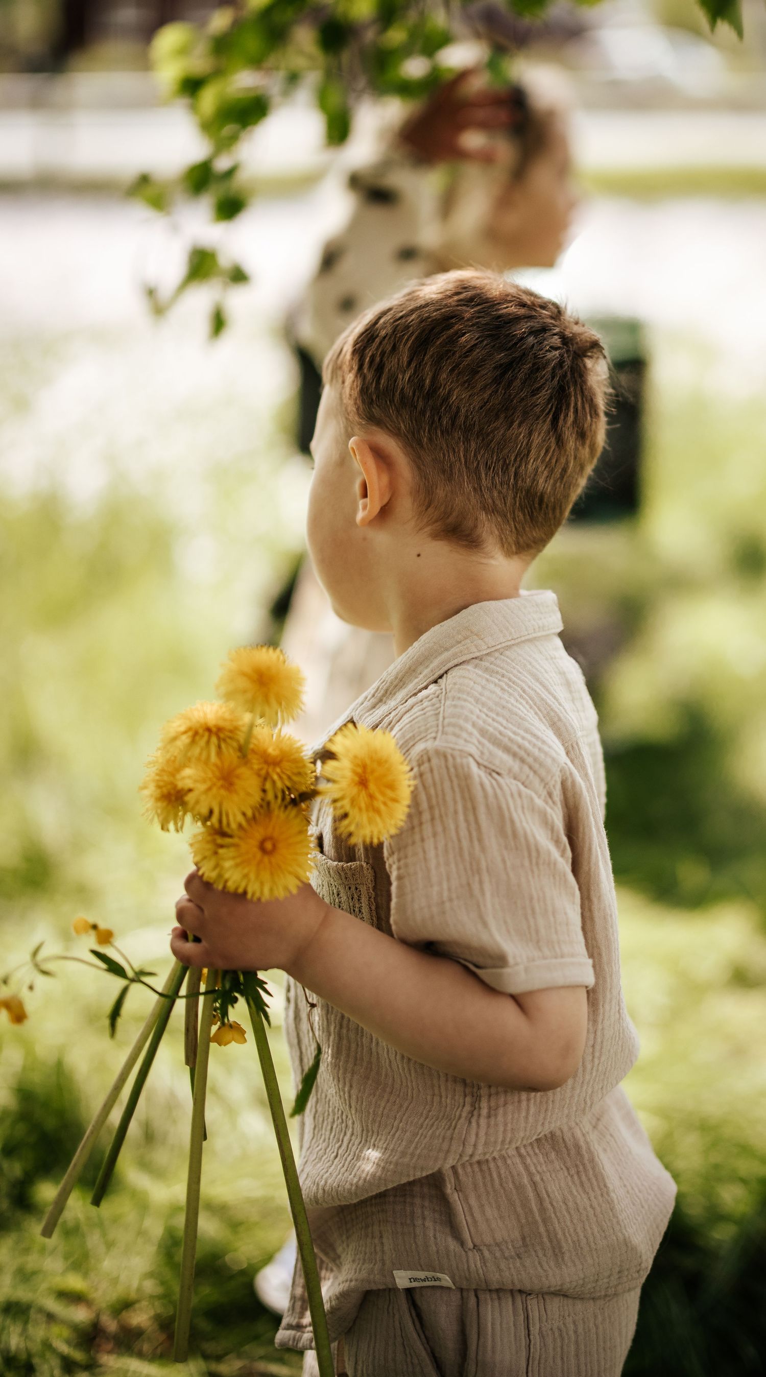 A young boy holding a bouquet of yellow dandelions in a lush green garden.