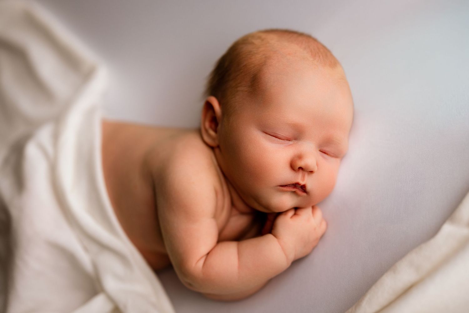 Sleeping newborn baby resting on a white blanket in a soft and serene professional studio portrait.